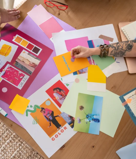 wo designers working on branding and photo editing, using a tablet and camera, with color palettes and printed photos on a desk.