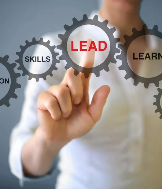 A person pointing at a digital interface with interconnected gears labeled 'LEAD,' 'SKILLS,' and 'LEARN,' representing leadership and professional development.