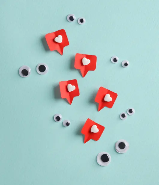 A creative illustration of social media engagement by Uzmate, featuring red like icons and googly eyes on a blue background.